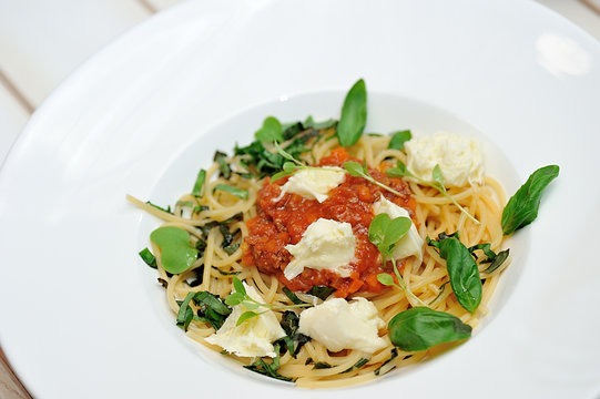 The image is very tasty spaghetti bolognese with cheese and basil on a white table.