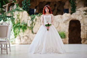 Fototapeta na wymiar Charming red-haired bride with wedding bouquet at hand posed at