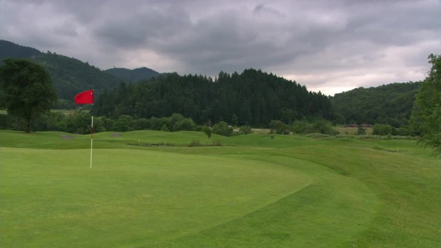 Left pan from hills under stormy sky to flag fluttering on a golf course