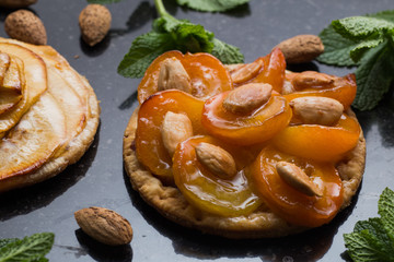 Tart with apricot and apple. Traditional french pie with fruits on dark marble background. Decorated almonds and mint leafs. Delicious dessert with copy space closeup.
