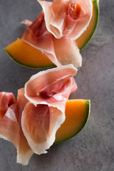 Jambon mix. Ham. Traditional Italian and Spanish salting, smoking, dry-cured dish - jamon Serrano and prosciutto crudo sliced with melon on grey background. Copy space. Closeup. 
