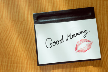 Sexy girl Red lips kiss and "Good Morning" word write on white note paper on bed stand table in the morning light. 
romantic message from couple.