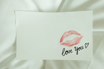 Sexy girl Red lips kiss and "love you" write on blank white note paper on white bed in the morning light. 
romantic message from couple. 