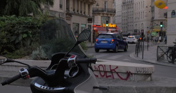 Logos and faces blurred. Car traffic on small street in the evening with motorbike in foreground