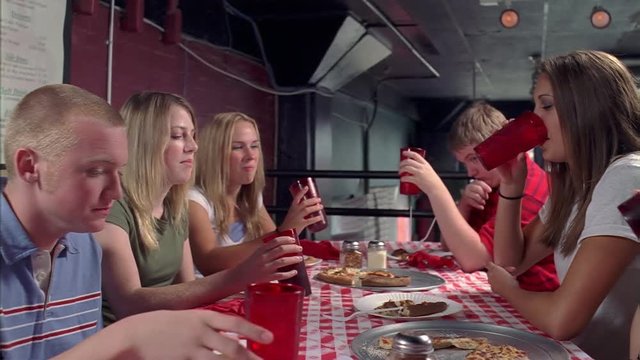 Teenagers sitting at long table in a pizza parlor