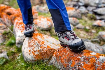trekking and hiking boots walking on the orange lichen covered stones. Concept of quality hiking shoes