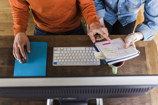 Two colleagues working at desk with computer and notepad