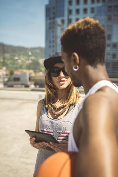 Young woman with digital tablet talking to basketball player