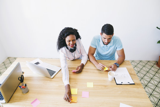 Young man and woman in office writing on adhesive notes on desk