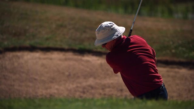 Golfer lofting ball out of a sand trap in ultra-slow motion
