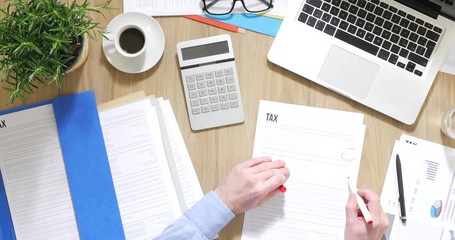 Businessman working at office desk, he is checking tax forms and using a calculator, top view