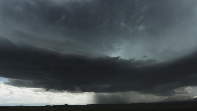 A mass of dark storm clouds sweeps ahead of pouring rain over the prairie, time lapse