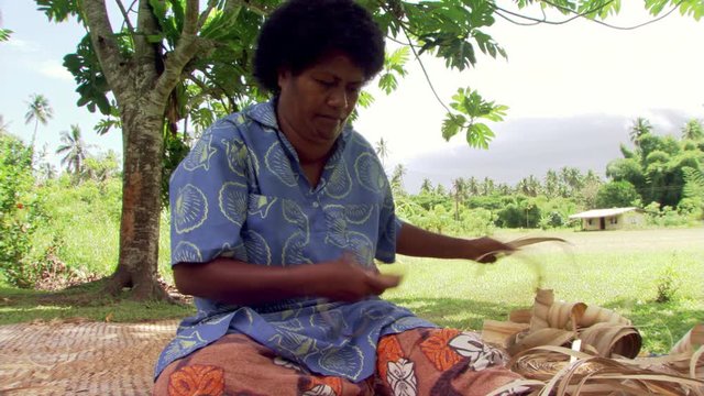 Fijian woman stripping bark and weaving it