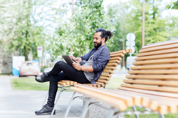 man with tablet pc sitting on city street bench