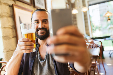 man with smartphone drinking beer at bar or pub