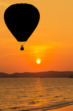 silhouette hot air balloon floating over tropical beach with sunset background