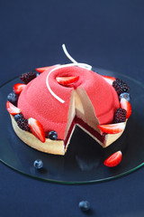 The inside of contemporary Summer Berry Mousse Cake covered with red velvet spray and decorated with fresh berries, on a dark blue background. 