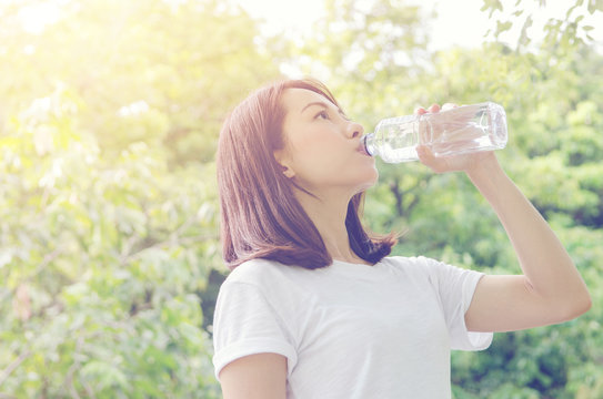 Young woman drinking water after jogging at summer green park. outdoor.