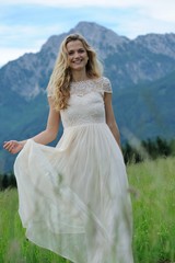Fototapeta na wymiar Junge Frau läuft in einem langen Kleid über eine Bergwiese im Berchtesgadener Land