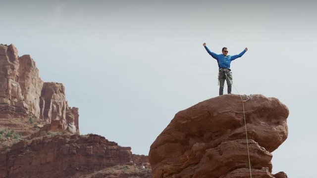 Wide low angle panning shot of man celebrating on rock formation / Fisher Towers, Utah, United States