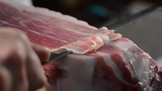 Butcher cuts a slice of Parma ham with a knife, close up on the slice and knife