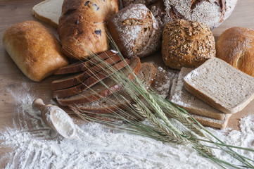 Verschiedene Brotsorten / Verschiedene Brotsorten und Getreideaehren auf einem Holztisch mit Mehl.