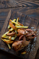 Wooden serving board with baked quails and potato wedges