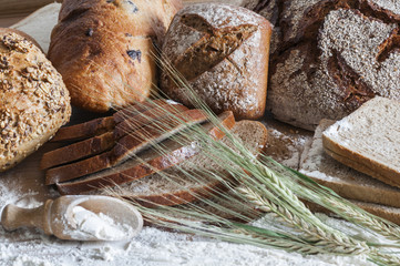 Verschiedene Brotsorten / Verschiedene Brotsorten und Getreideaehren auf einem Holztisch mit Mehl.