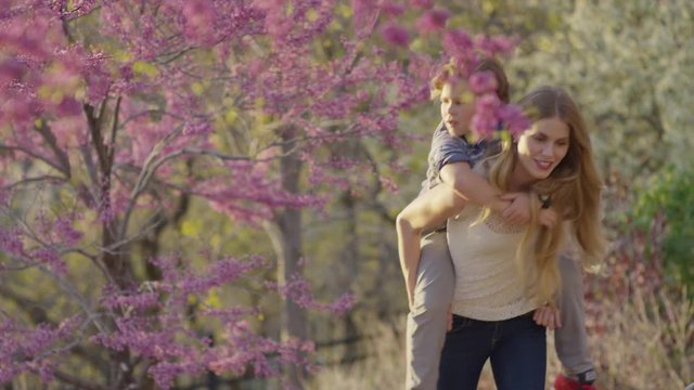 Medium panning shot of mother carrying son piggyback in park / Cedar Hills, Utah, United States