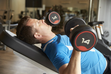 Fototapeta na wymiar Man works out with dumbbells on a bench at a gym, side view