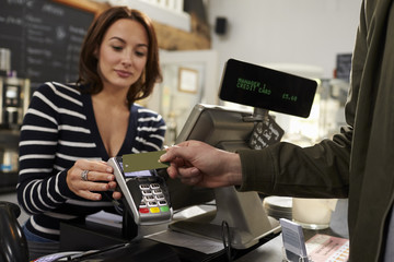 Customer making a contactless card payment over shop counter - obrazy, fototapety, plakaty
