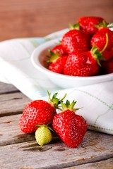 Green strawberry with red ones next to bowl