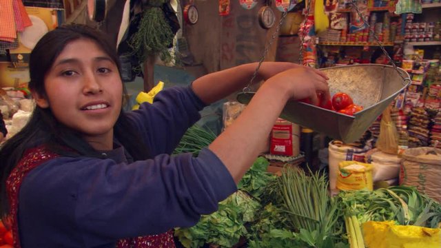 Young Peruvian woman weighing tomatoes at a produce market