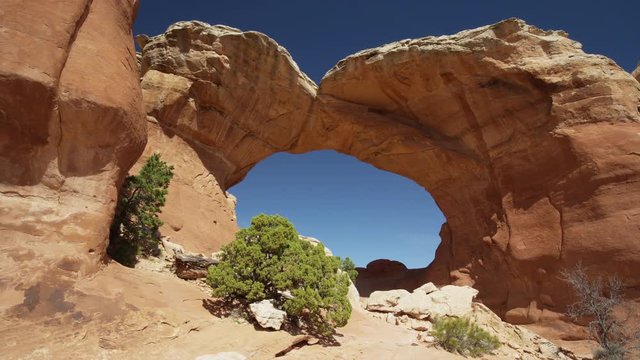 Wide low angle panning shot of arch in desert landscape / Arches National Park, Utah, United States