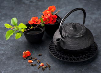 Obraz na płótnie Canvas Black iron asian style teapot and cup green tea and flowers on black grunge background