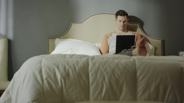 Medium shot of man using digital tablet on bed / Cedar Hills, Utah, United States
