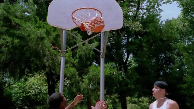 Teenage boy making a successful jump shot on an outdoor basketball court