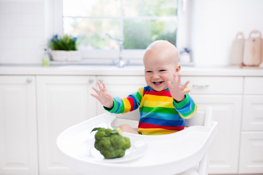 Little boy eating broccoli in white kitchen