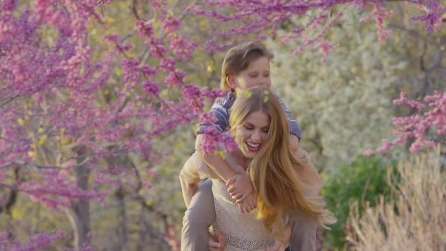 Medium panning shot of mother carrying son piggyback in park / Cedar Hills, Utah, United States