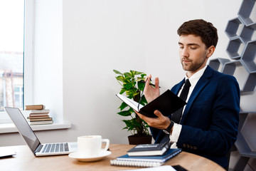 Fototapeta premium Young successful businessman sitting at workplace, office background.