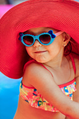The beautiful little girl in a bathing suit and a hat swims in t