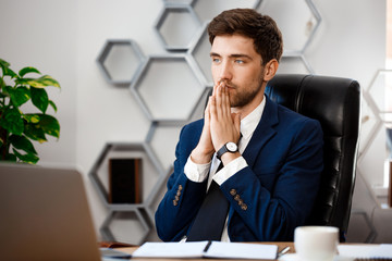 Young successful businessman sitting at workplace, office background.