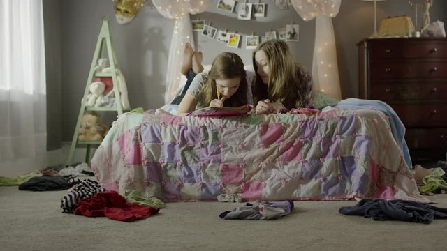 Medium shot of teenage girls doing homework on bed / Cedar Hills, Utah, United States