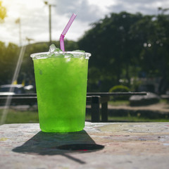 fresh Green soda iced in a big plastic glass with pink tube in the park with shadow of glass, day light, sunlight, light effect added