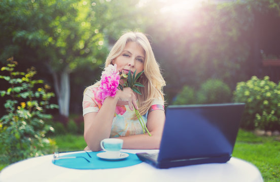 Красивая блондинка за чашкой кофе и ноутбуком в саду