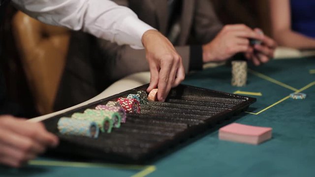 The dealer at the poker table lays chips under par. the game of poker. A croupier in a casino at a poker table arranges the chips according to the value. Close-up of hands of the dealer.