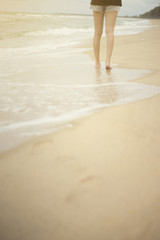 Beach travel - young woman walking on sand beach leaving footprints in the sand,filtered image, selective focus on woman,warm white balance picture style,light effect added