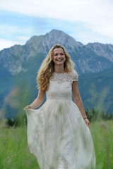 Fototapeta na wymiar Junge Frau im langen Sommerkleid auf einer Bergwiese vor dem Hochstaufen im Berchtesgadener Land
