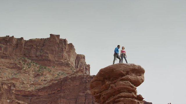 Wide low angle panning shot of couple standing on rock formation / Fisher Towers, Utah, United States