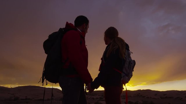 Medium panning shot of silhouette of couple holding hands / Moab, Utah, United States